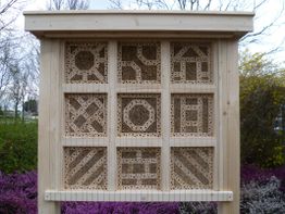 Insektenhotel aus Holz mit geometrischen Mustern in neun Abschnitten, umgeben von Natur.
